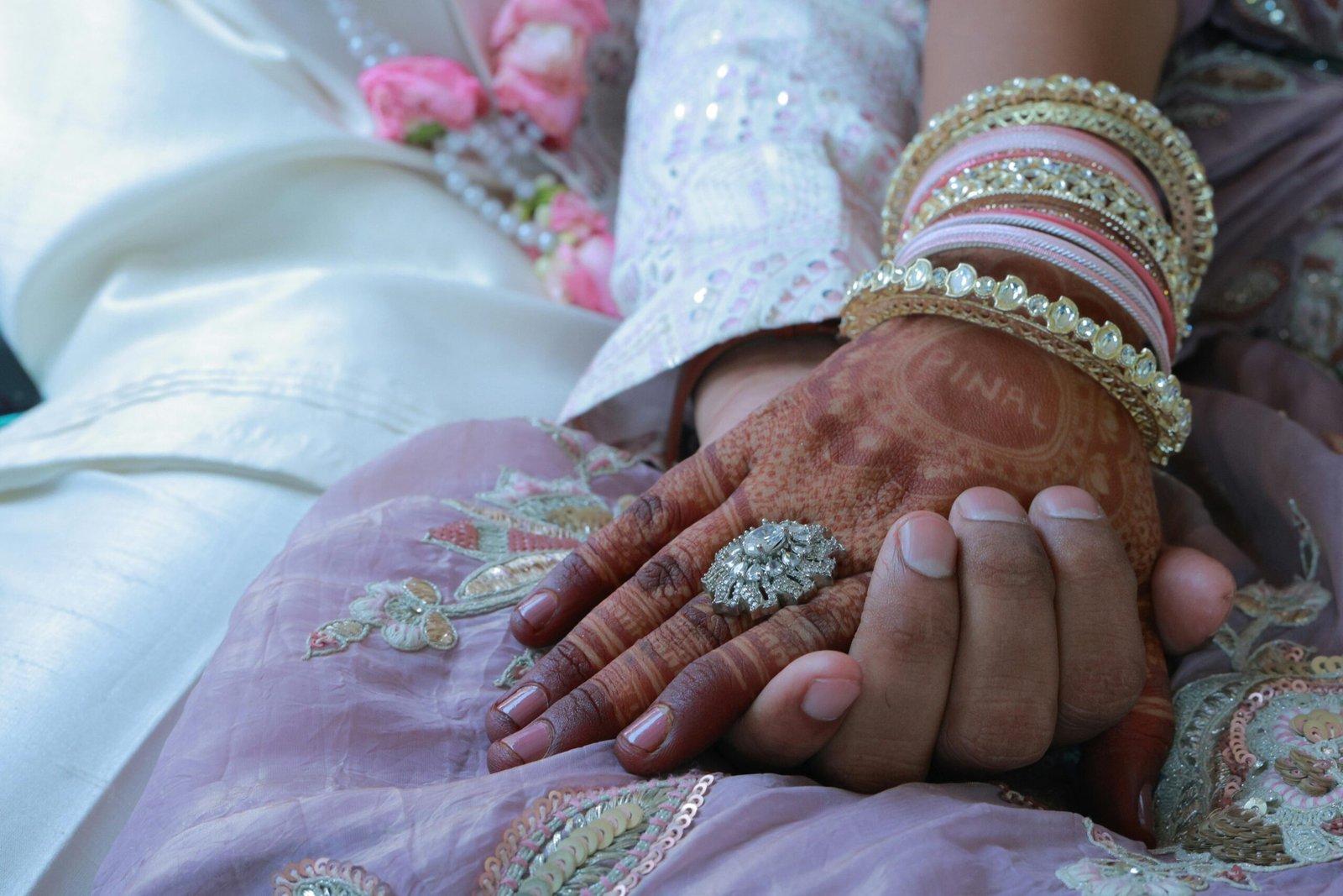 Close-up of a couple's hands adorned with henna and jewelry, symbolizing love and unity in an Indian wedding.